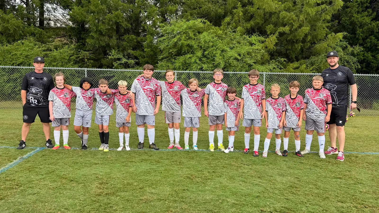 The Rogue Raiders U11 squad lined up arm in arm on the field with their coaches.